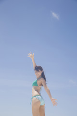 青空に両手を挙げる水着女性