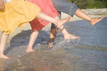 波を足で蹴りはしゃぐ女性2人と男性の足元