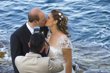 Fotografo con gli sposi che si baciano in riva al mare