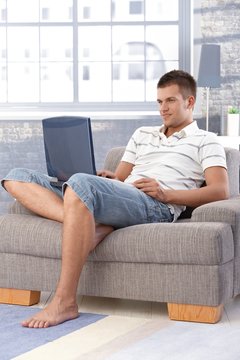 Young man using laptop at home smiling