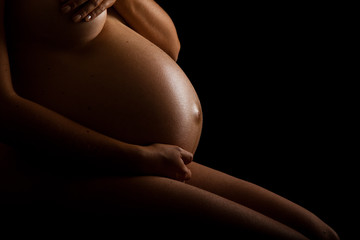 Nude pregnant woman belly on black background
