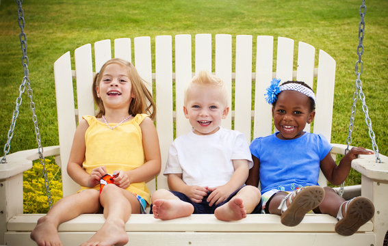 Three Cute Little Kids Laughing Together On A Porch Swing