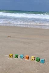 The word WELCOME written on colorful wood cubes, at the beach