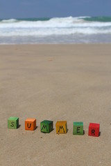 The word SUMMER - written on colorful wood cubes, at the beach