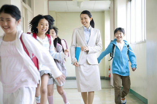 廊下を歩く女性教師とはしゃぐ小学生男女