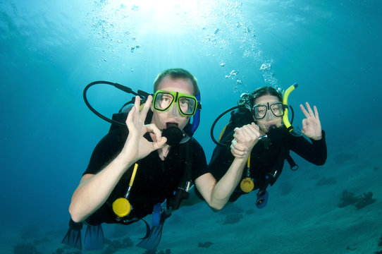 Scuba divers, man and woman give OK sign underwater