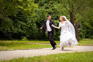 happy bride and bridegroom running along the alley in the park
