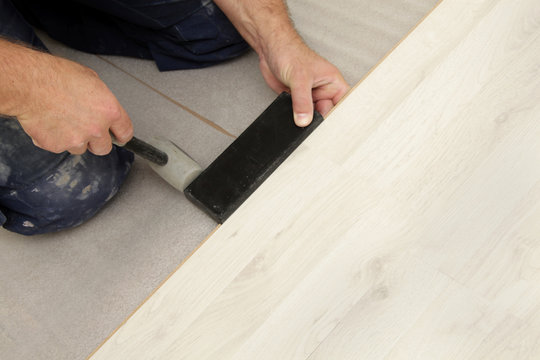 homme posant parquet flottant stratifi&eacute; avec marteau