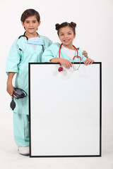 Children dressed up as doctors and standing behind a blank sign