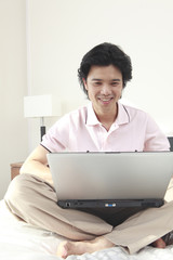 ベッドの上でノートパソコンに向かう男性