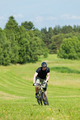 Obraz premium Sportive man mountain biking uphill sunny meadows