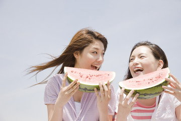 砂浜で西瓜を食べる2人の女性