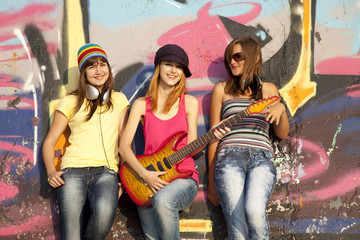 Three beautiful girls with guitar and graffiti wall at backgroun