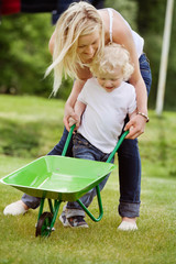 Mother helping her kid in pushing wheelbarrow