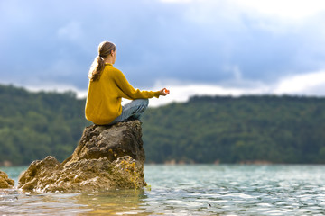 Meditierender Mann auf einem Stein am See