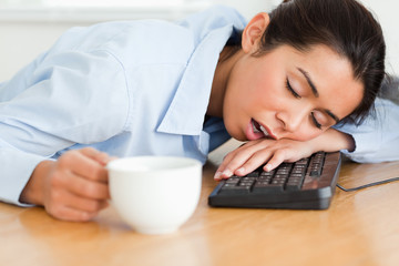 Pretty woman sleeping on a keyboard while holding a cup of coffe