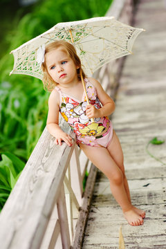 cute little girl in swimsuit with sun umbrella taking sunbathe