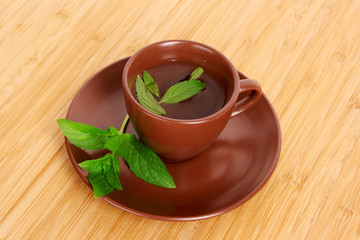 Cup of green tea on the saucer with mint on wooden surface