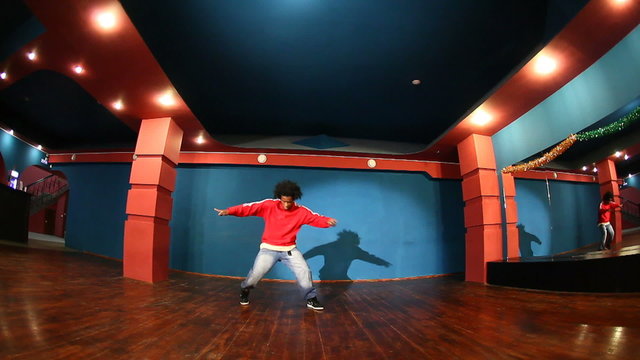 Wide shot of young African American guy performing modern hip hop dance in studio. Ideal for music videos, youth culture, street style choreography and entertainment content