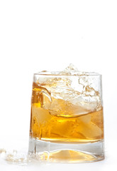 glass of whiskey with ice cubes splashing out over white