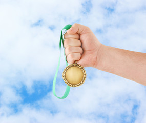 Gold medal in hand on sky background