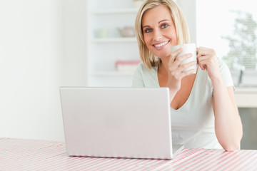 Close up of a woman holding coffee with laptop in front of her s