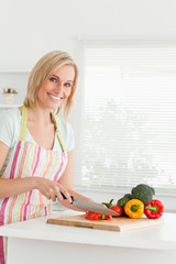 Gorgeous woman cutting red pepper looks into camera