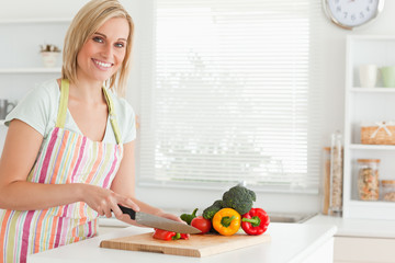 Cute woman cutting red pepper looks into camera
