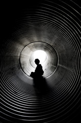 The silhouette of sitting boy with light at the end of tunnel