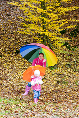 mother and her daughter with umbrellas in autumnal nature