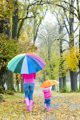 mother and her daughter with umbrellas in autumnal alley