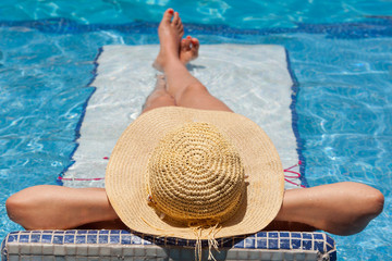 Woman in hat relaxing on holiday on swimming pool bed