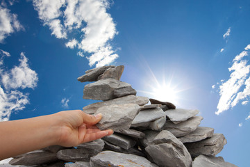 Woman adds rock to cairn under sun filled sky