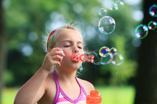 little girl blowing soap bubble outdoor