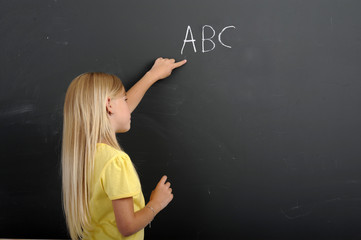 girl writing ABC on a chalkboard