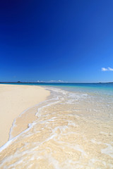 Fototapeta na wymiar 真っ白な砂浜に打ち寄せる波と青い空
