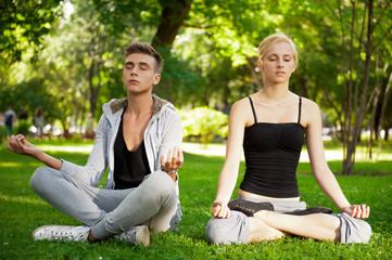 Portrait of young beautiful couple sitting in lotus pose on gree