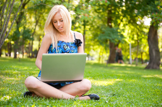 Beautiful student woman with a laptop sitting on green grass at