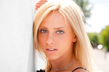 Portrait of pretty young woman standing outdoors near white wall