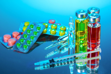 medical ampoules, tablets and syringe on blue background