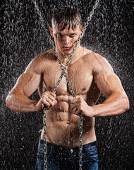 Wet muscle sexy young man posing under the rain in studio