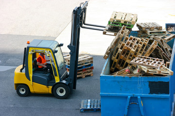 Worker collects wood pallets for recycling