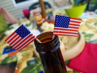Two American flags planted in the top of a beer bottle at picnic