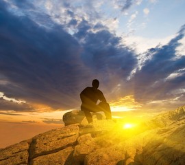 man sitting on a mountain top at the sunset