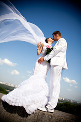 newly married couple kissing.wind lifting white bridal veil