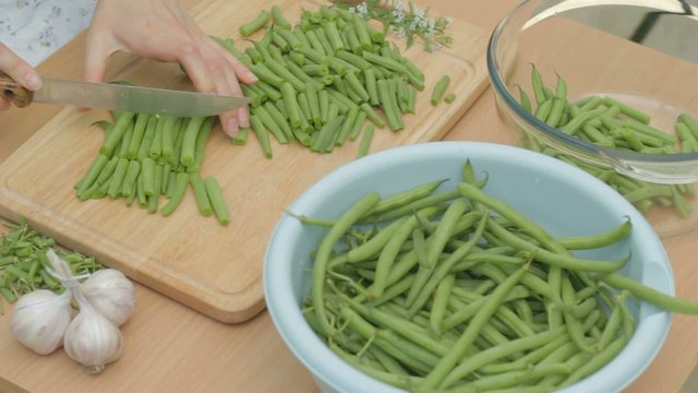 Slicing fresh green string beans on wooden chopping board
