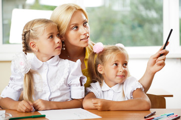 Fototapeta na wymiar Young pretty teacher helping her little students in classroom