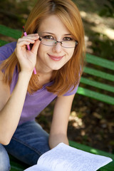 Obraz premium Redhead girl in glasses doing homework at the park.