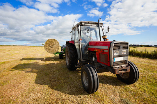 tractor collecting a roll of haystack in the field