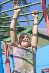 Fototapeta premium Little European girl hangs on horizontal bar